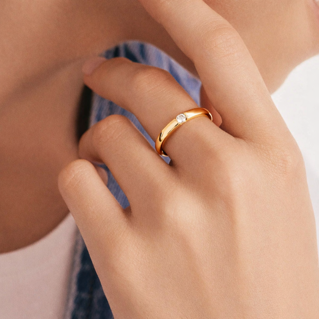 Close-up of a hand wearing a gold ring with a diamond on a blurred background