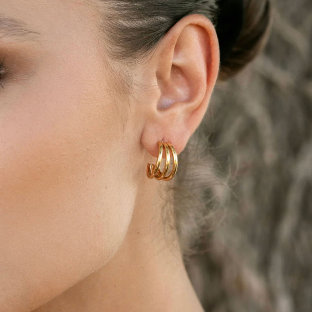 Close-up of a person wearing gold hoop earrings with a blurred background