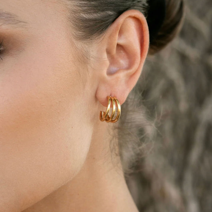 Close-up of a person wearing gold hoop earrings with a blurred background