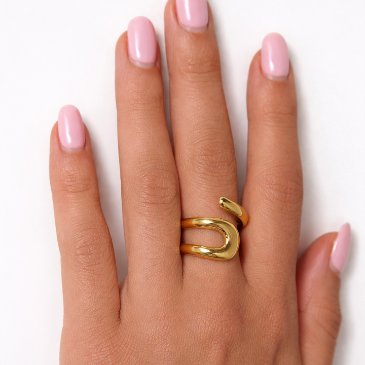 Hand wearing a gold ring with pink nail polish on a white background