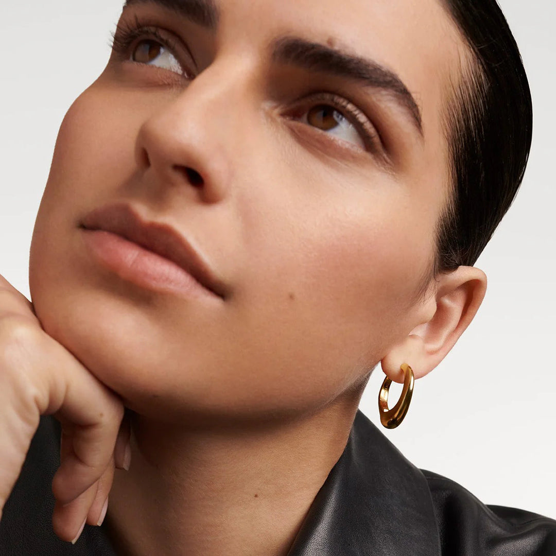 Close-up of a woman wearing gold hoop earrings with a neutral background
