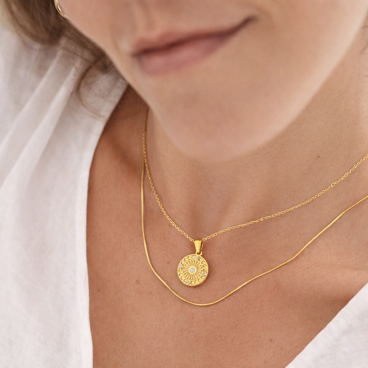 Close-up of a person wearing a gold necklace with a circular pendant.