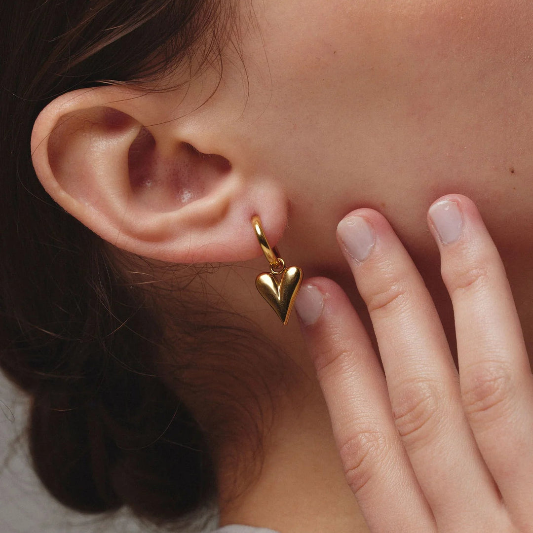 Close-up of a person wearing a gold heart-shaped earring.