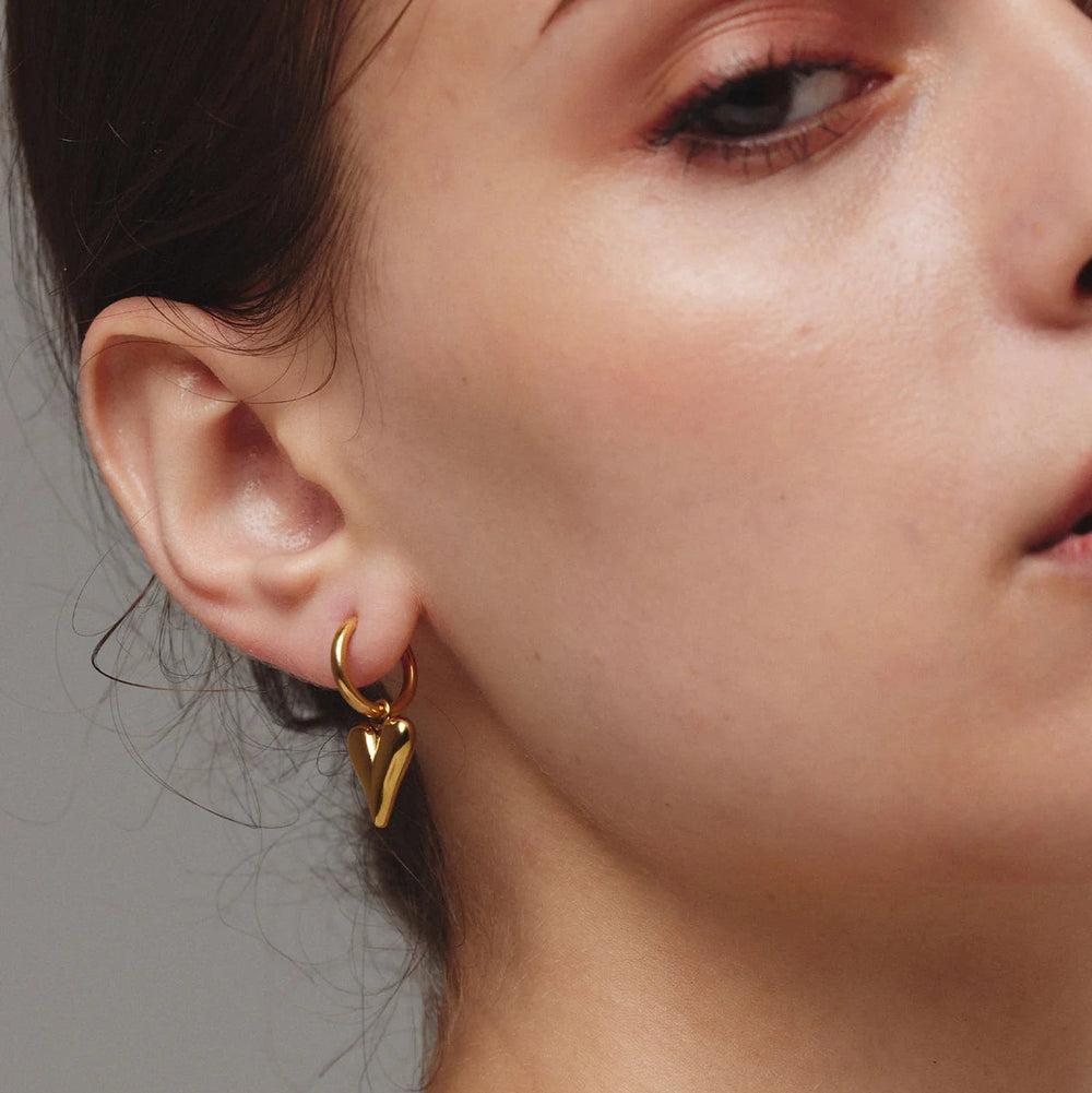 Close-up of a person wearing gold earrings with a neutral background