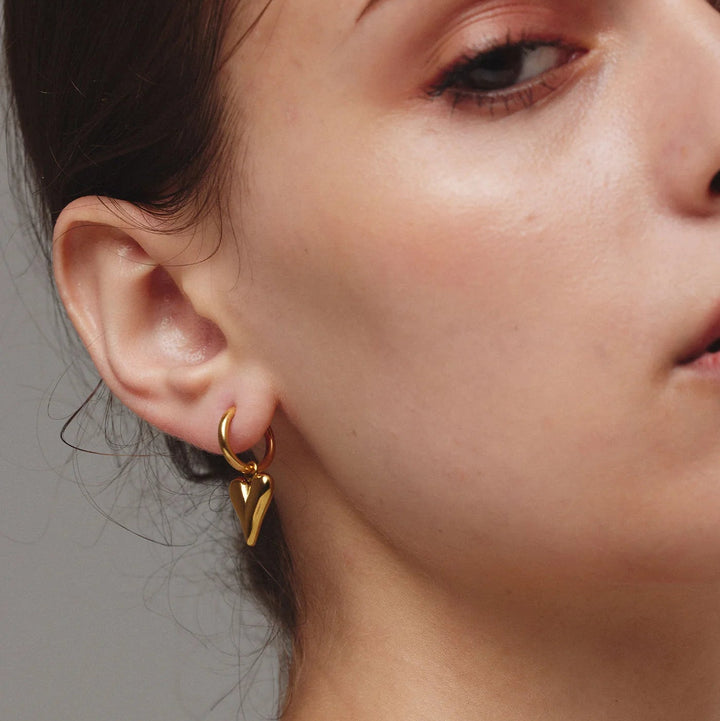 Close-up of a person wearing gold earrings with a neutral background