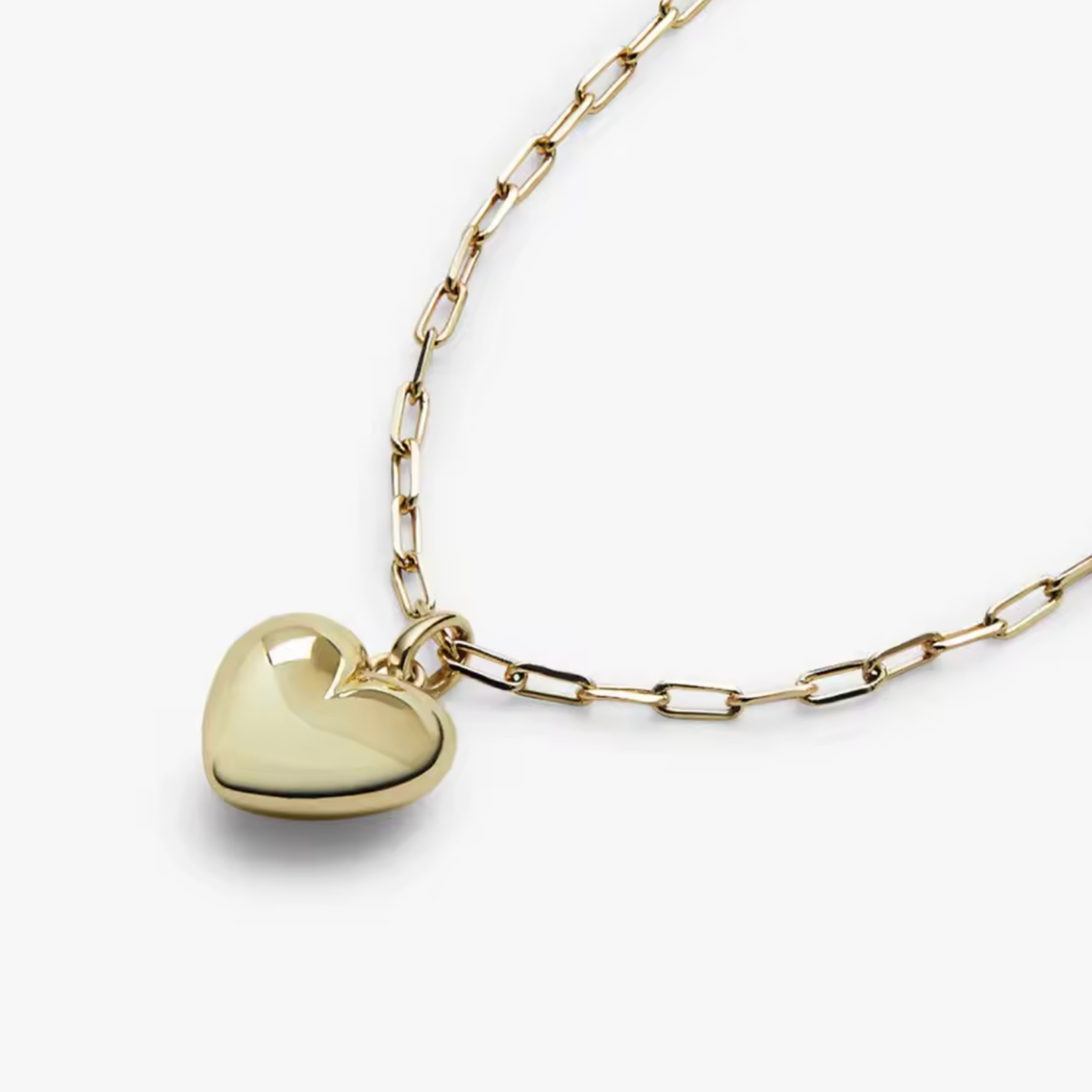 A polished gold heart pendant necklace on a gold paperclip chain, photographed on a clean white background.