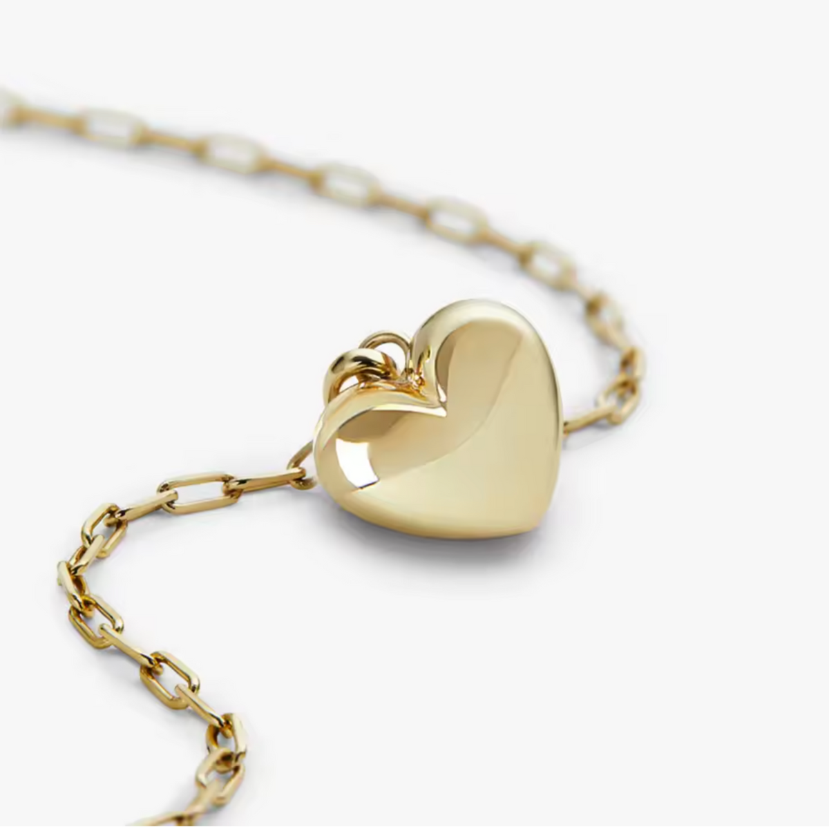 A polished gold heart-shaped pendant necklace on a matching gold chain, photographed on a clean white background.