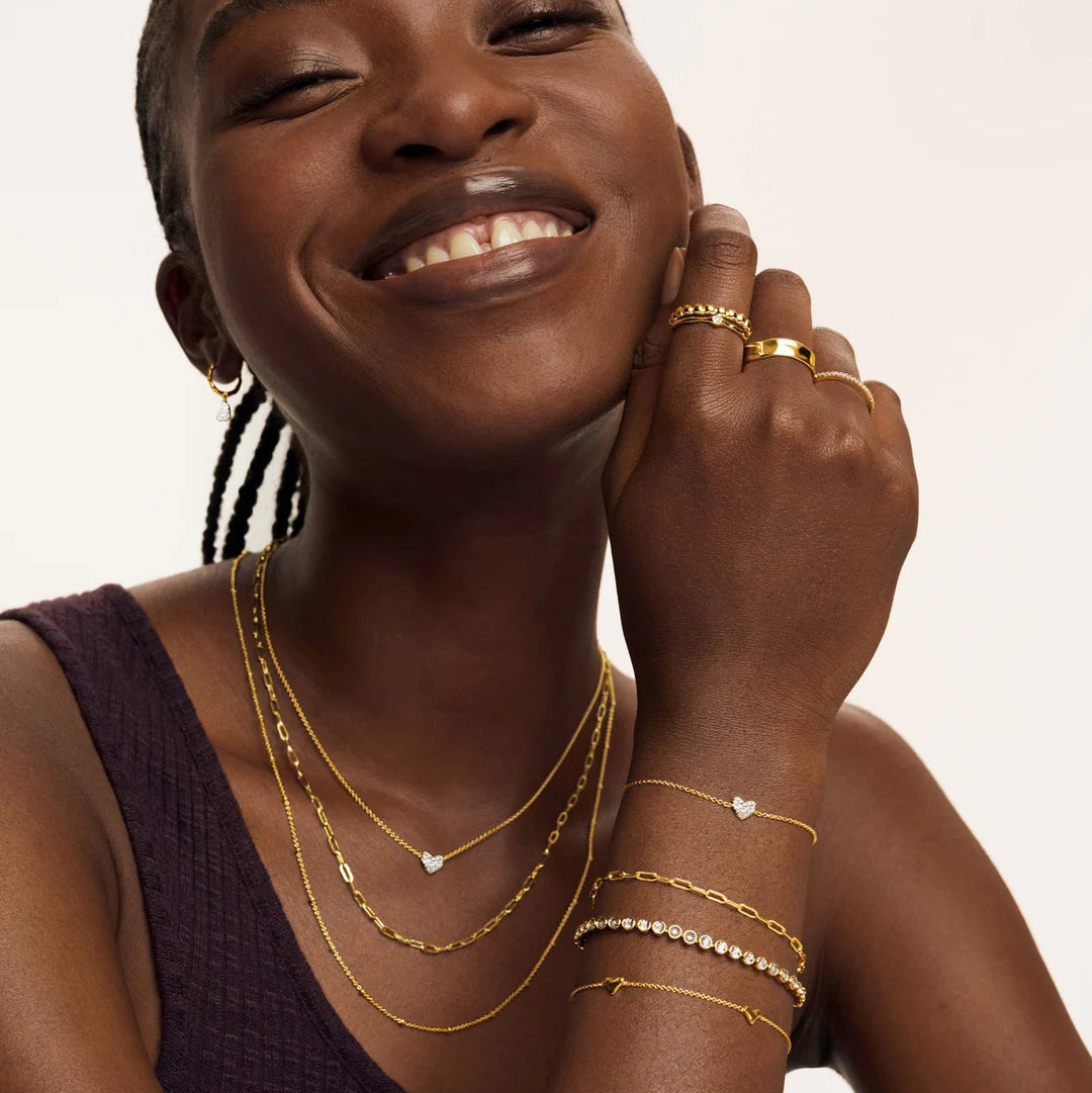 Woman wearing gold jewelry including necklaces, bracelets, and a ring on a plain background