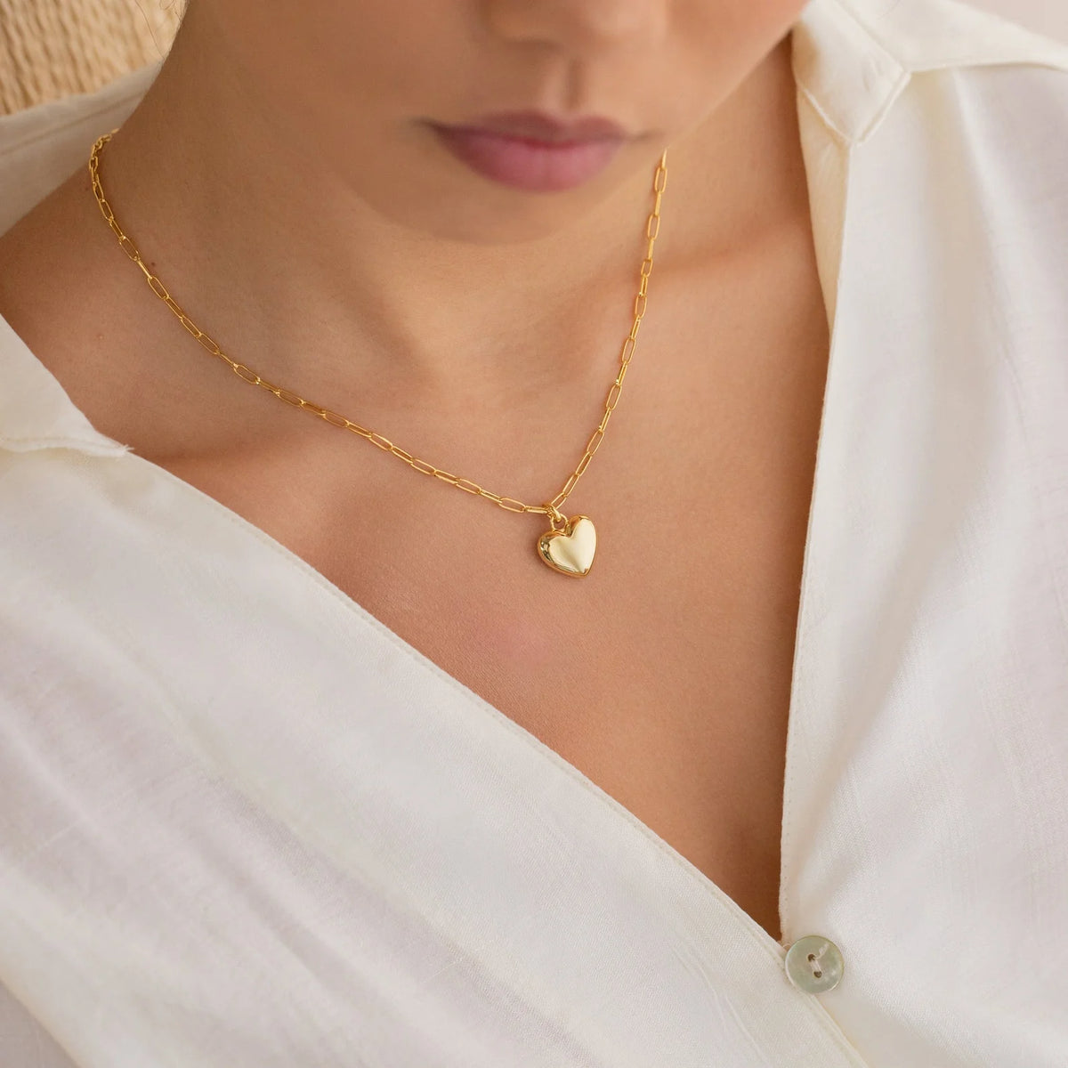 Gold necklace with a heart pendant worn by a person in a white shirt.