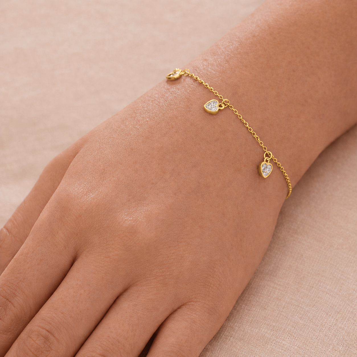 Gold bracelet with heart-shaped charms on a wrist against a beige background