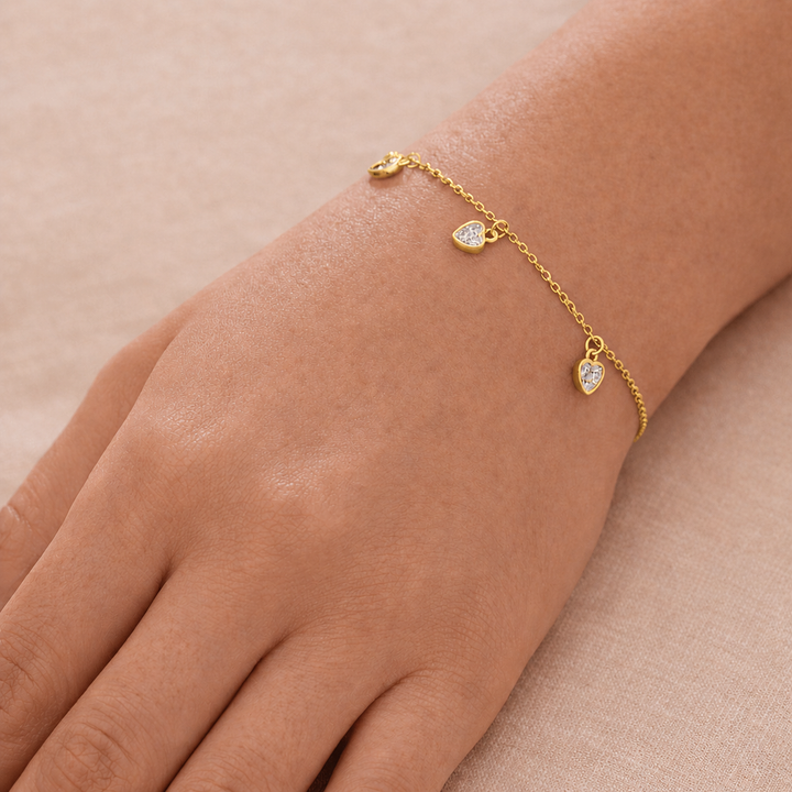 Gold bracelet with heart-shaped charms on a wrist against a beige background