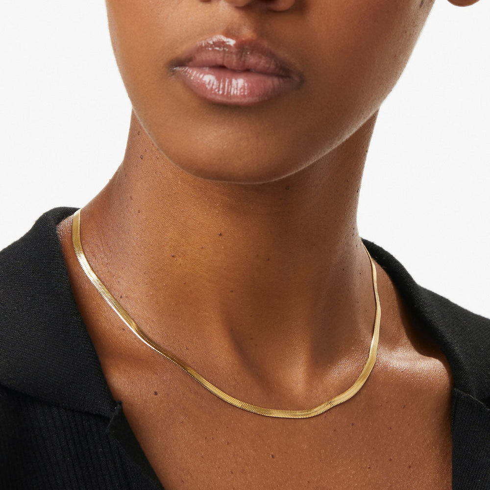 Close-up of a person wearing a gold necklace against a neutral background