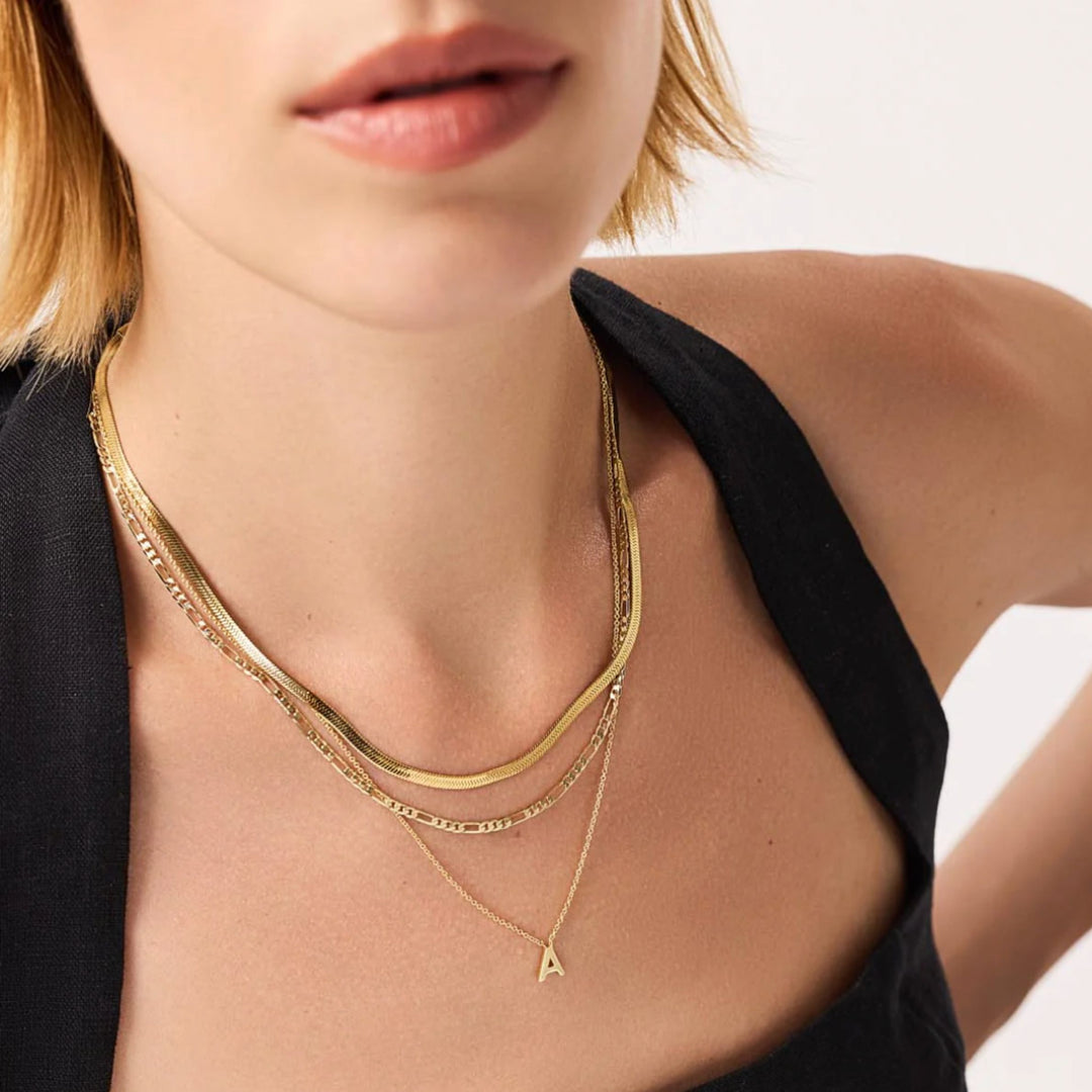 Close-up of a person wearing two gold necklaces with a plain background