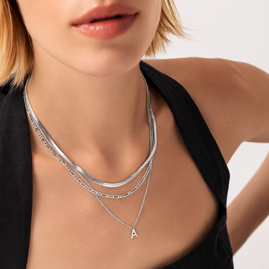 Close-up of a woman wearing two silver necklaces with a triangle pendant on a neutral background
