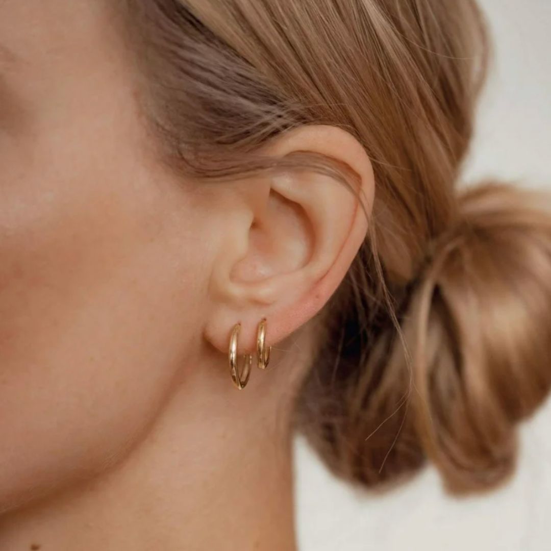 Close-up of an ear wearing gold hoop earrings with a blurred background