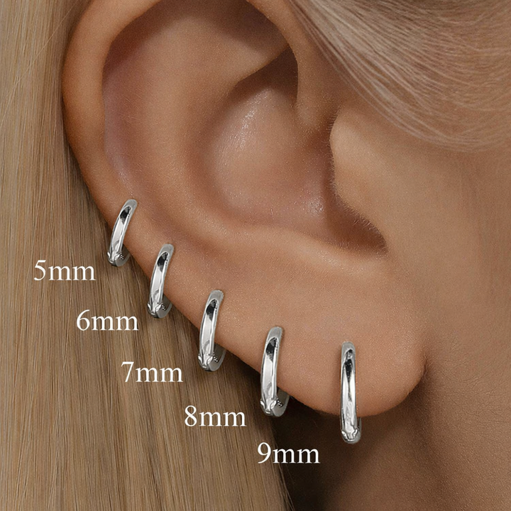 Silver hoop earrings of different sizes displayed on an ear.