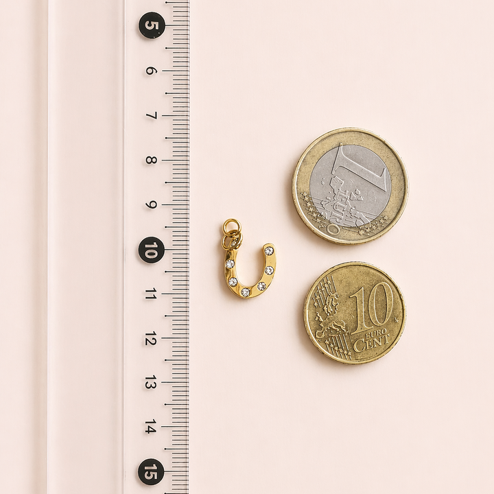 Gold earring and coins next to a ruler on a pink background