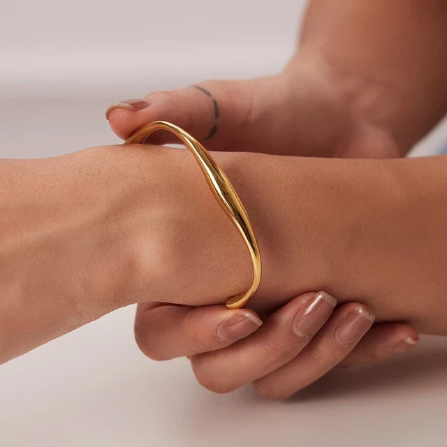 Gold bracelet on a wrist with a neutral background
