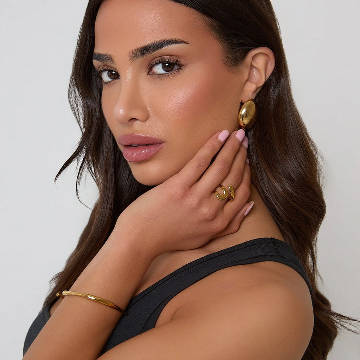 Woman wearing gold earrings and rings on a plain background