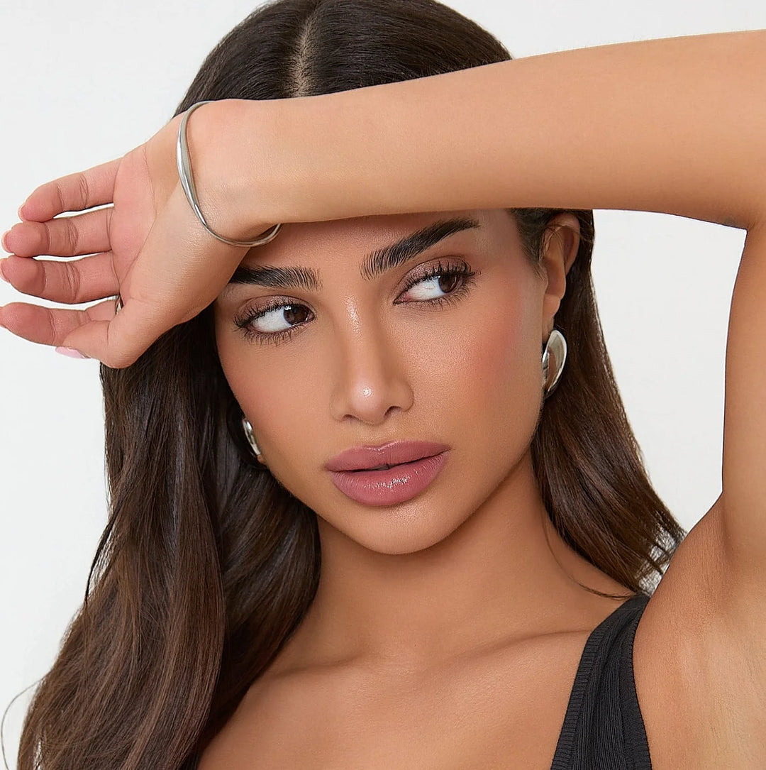 Woman with long brown hair and makeup, wearing a black top against a white background