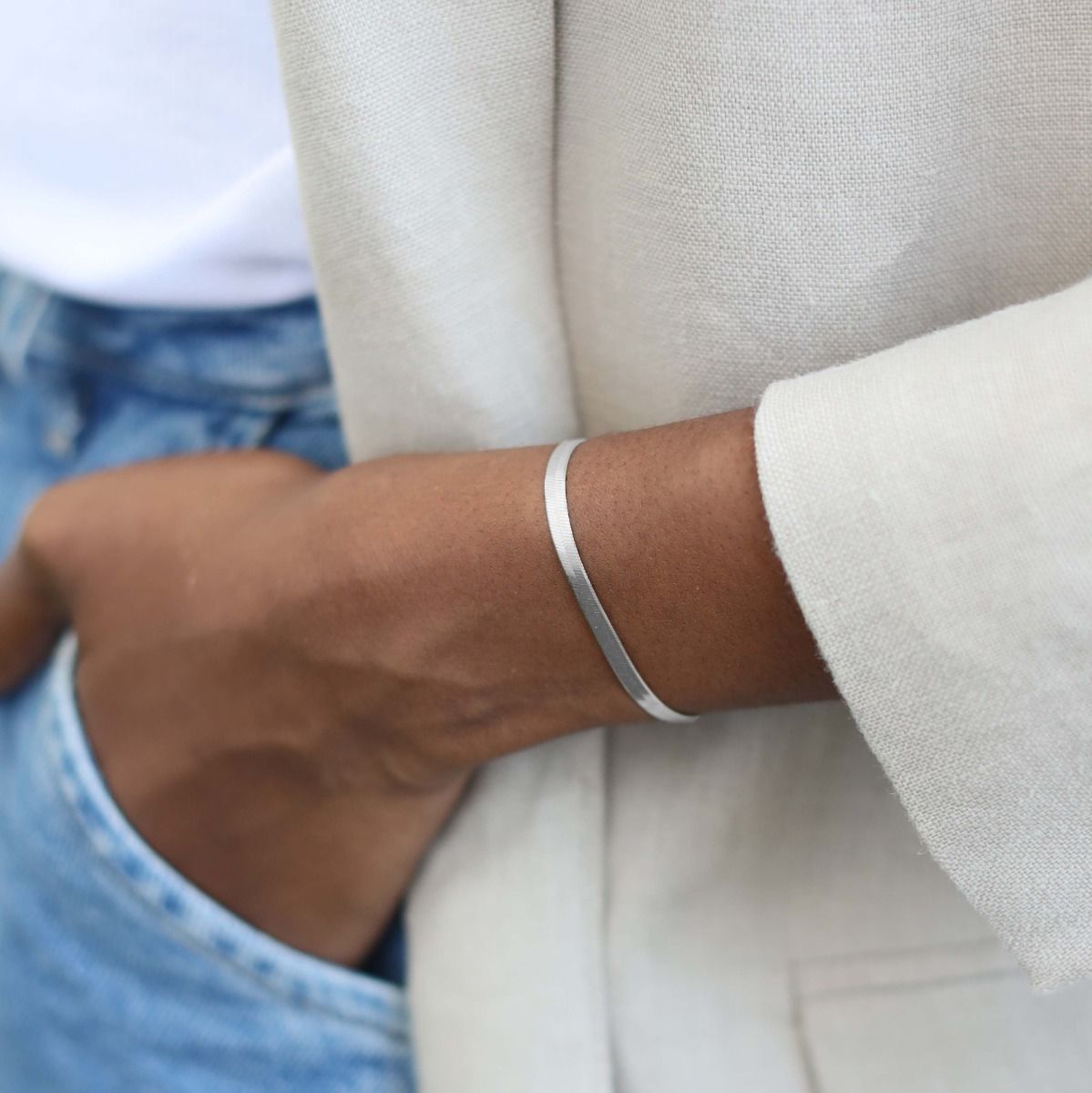 Close-up of a person wearing a silver bracelet on a neutral background