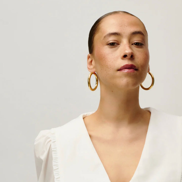 Woman wearing gold hoop earrings against a plain background
