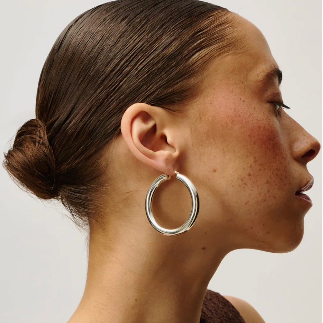Close-up of a person wearing a silver hoop earring with a plain background