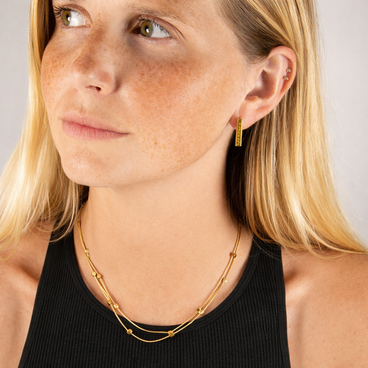 Close-up of a woman wearing a gold layered necklace against a neutral background
