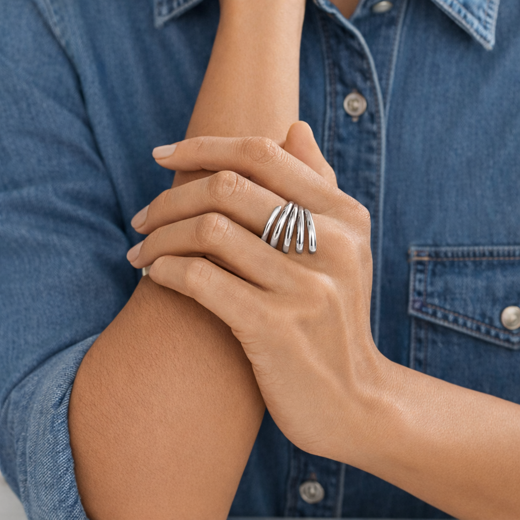 Hand wearing a silver ring with multiple bands against a denim background