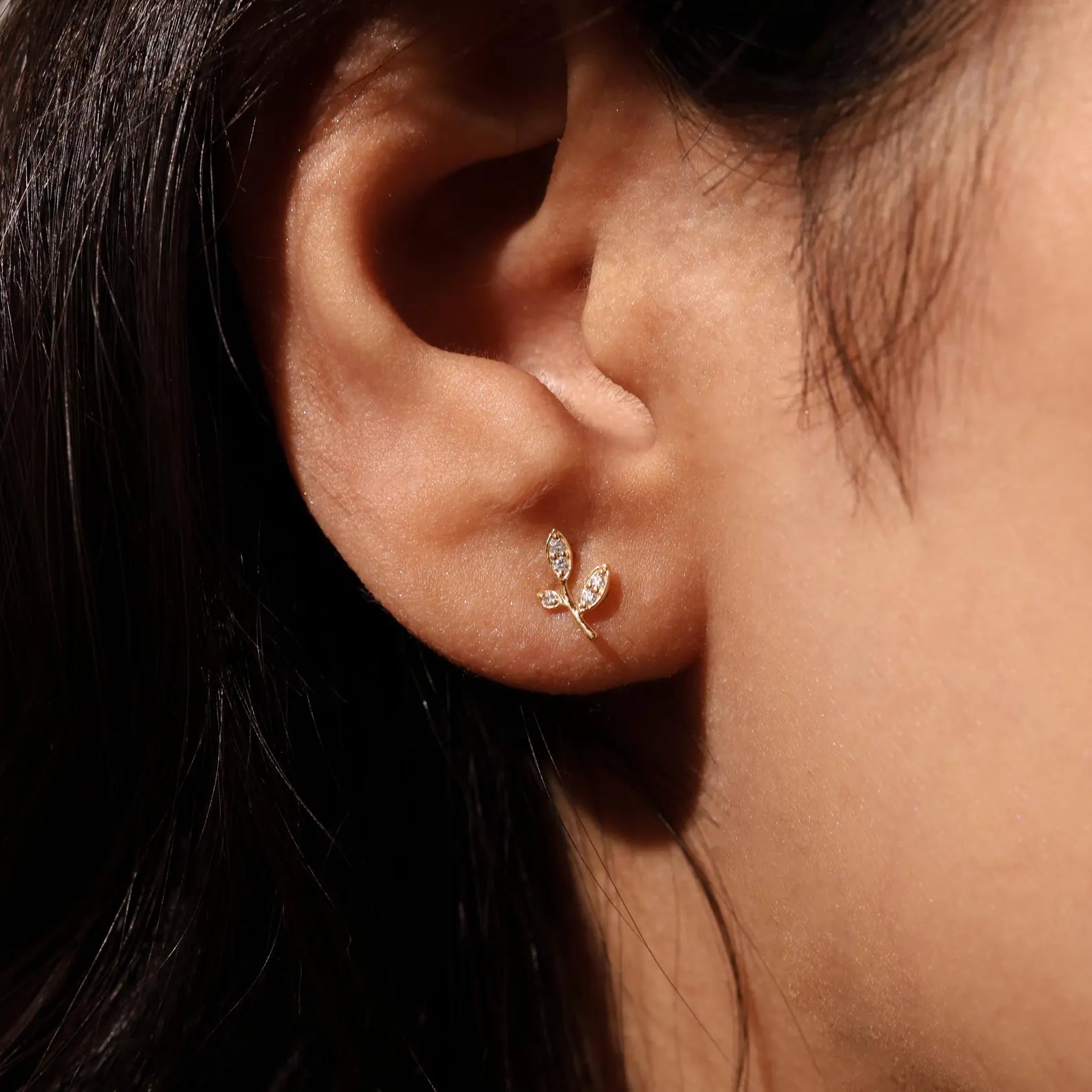 Close-up of an ear wearing a delicate earring with leaves.