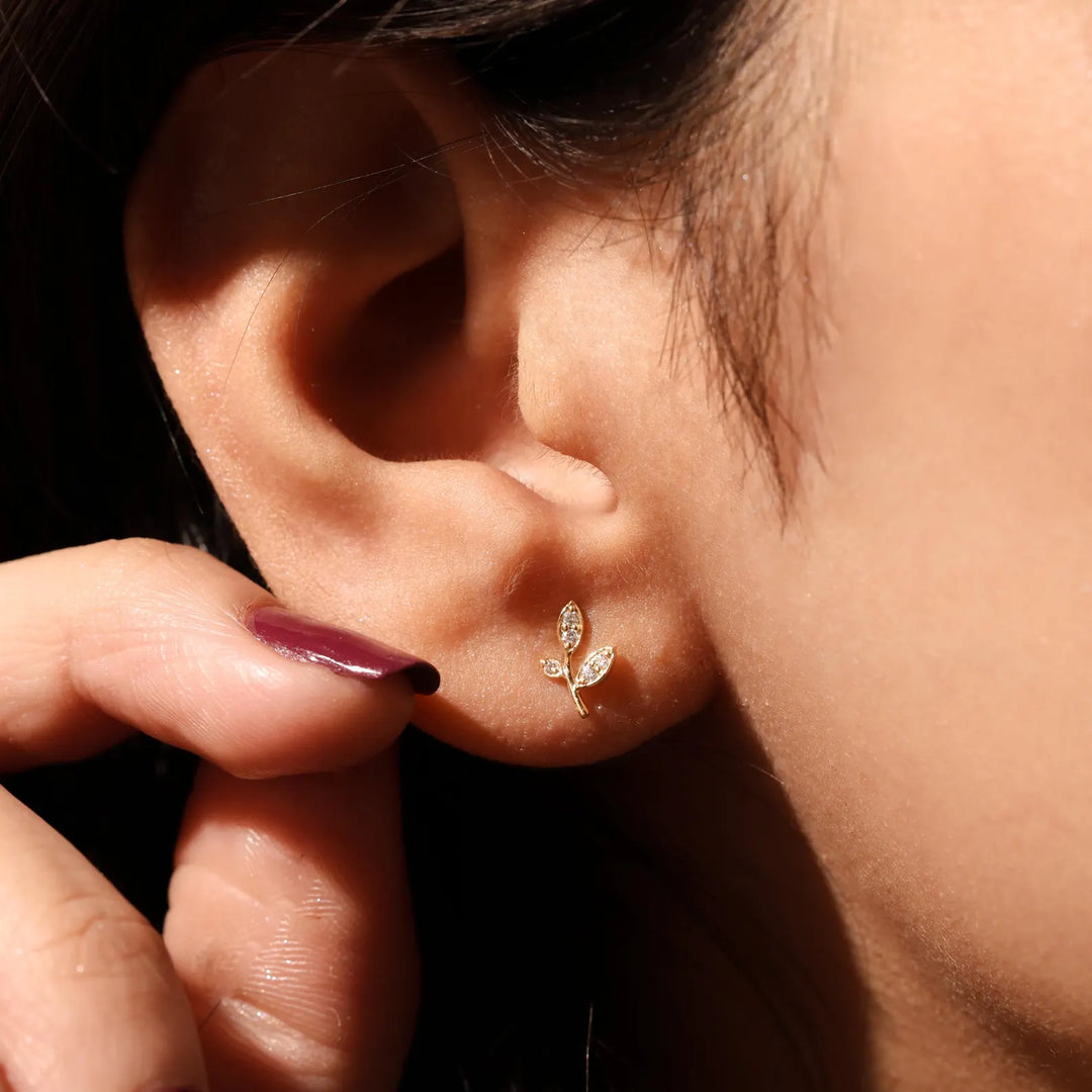 Close-up of an ear wearing a delicate gold earring with a hand adjusting it.
