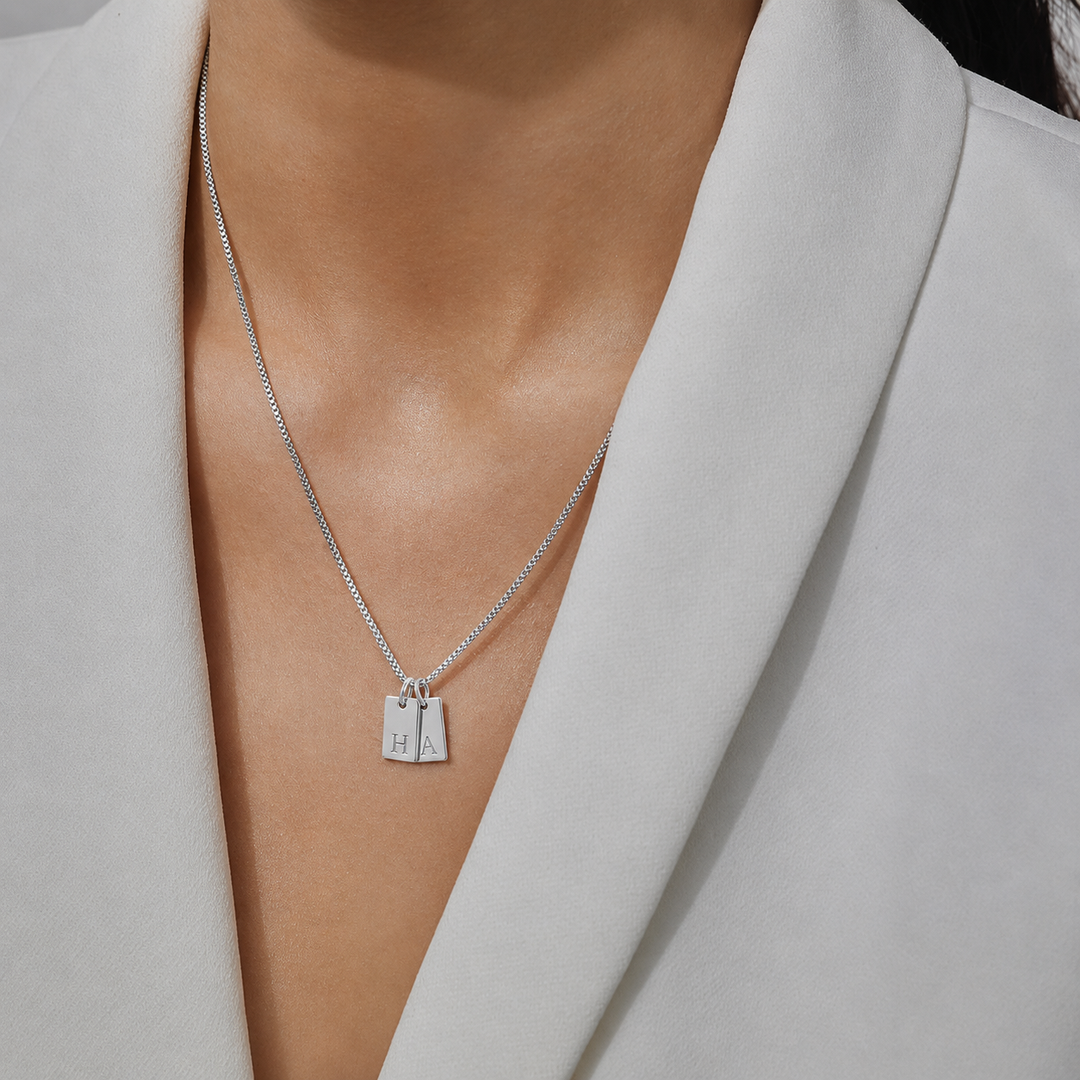 Silver necklace with a pendant on a person wearing a light gray blazer.