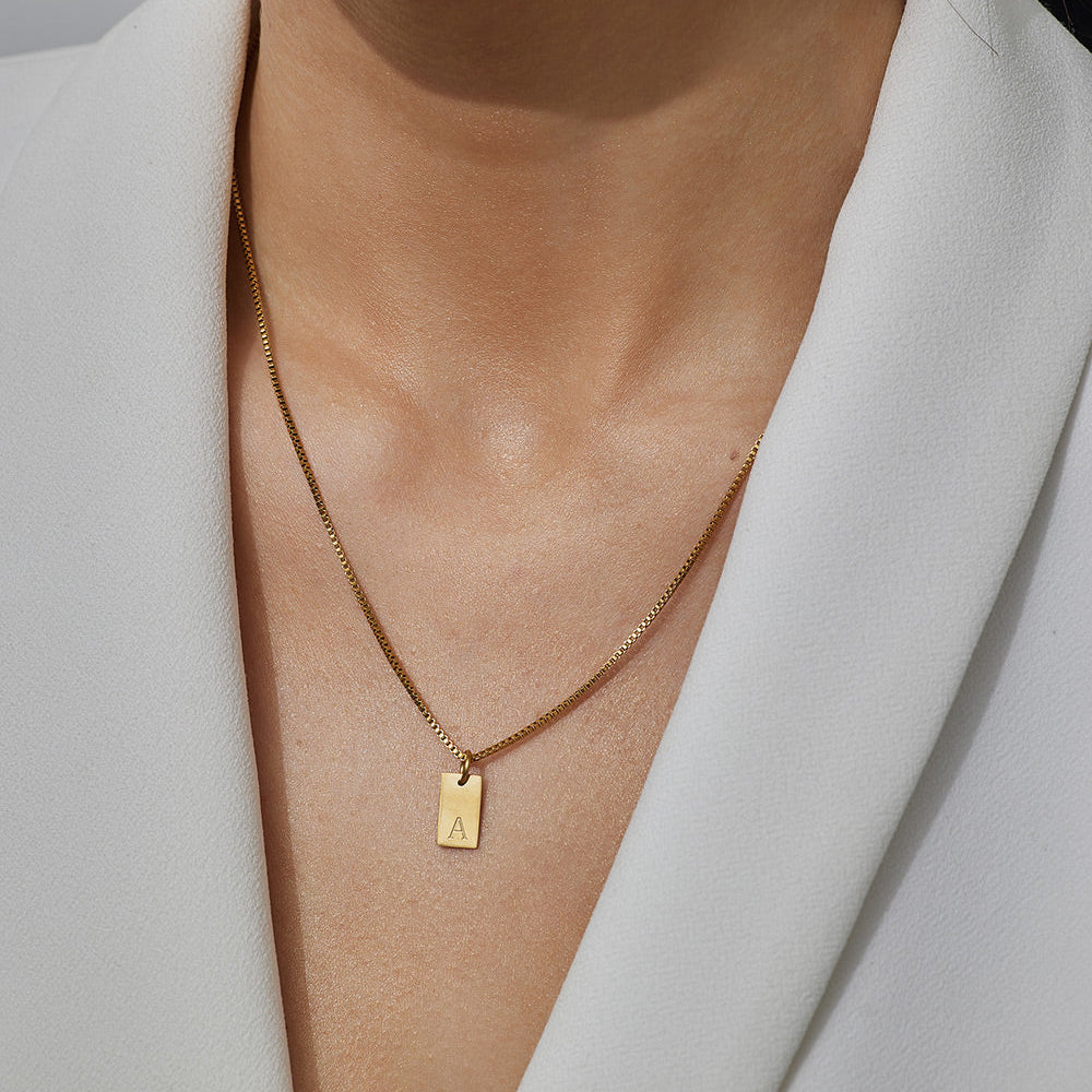 Gold necklace with a pendant worn by a person in a white blazer.