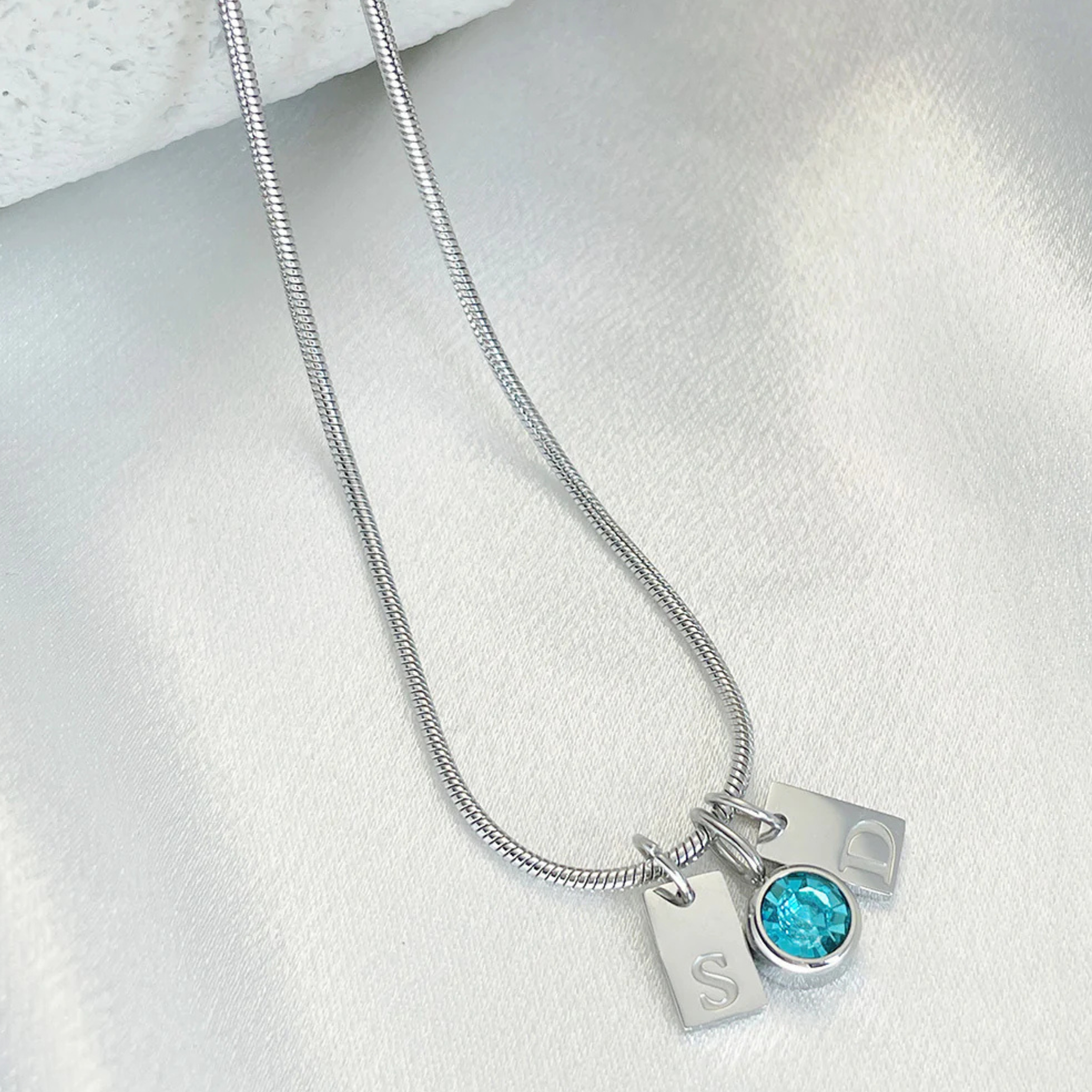 Silver necklace with a blue gemstone pendant and two charms on a light gray background