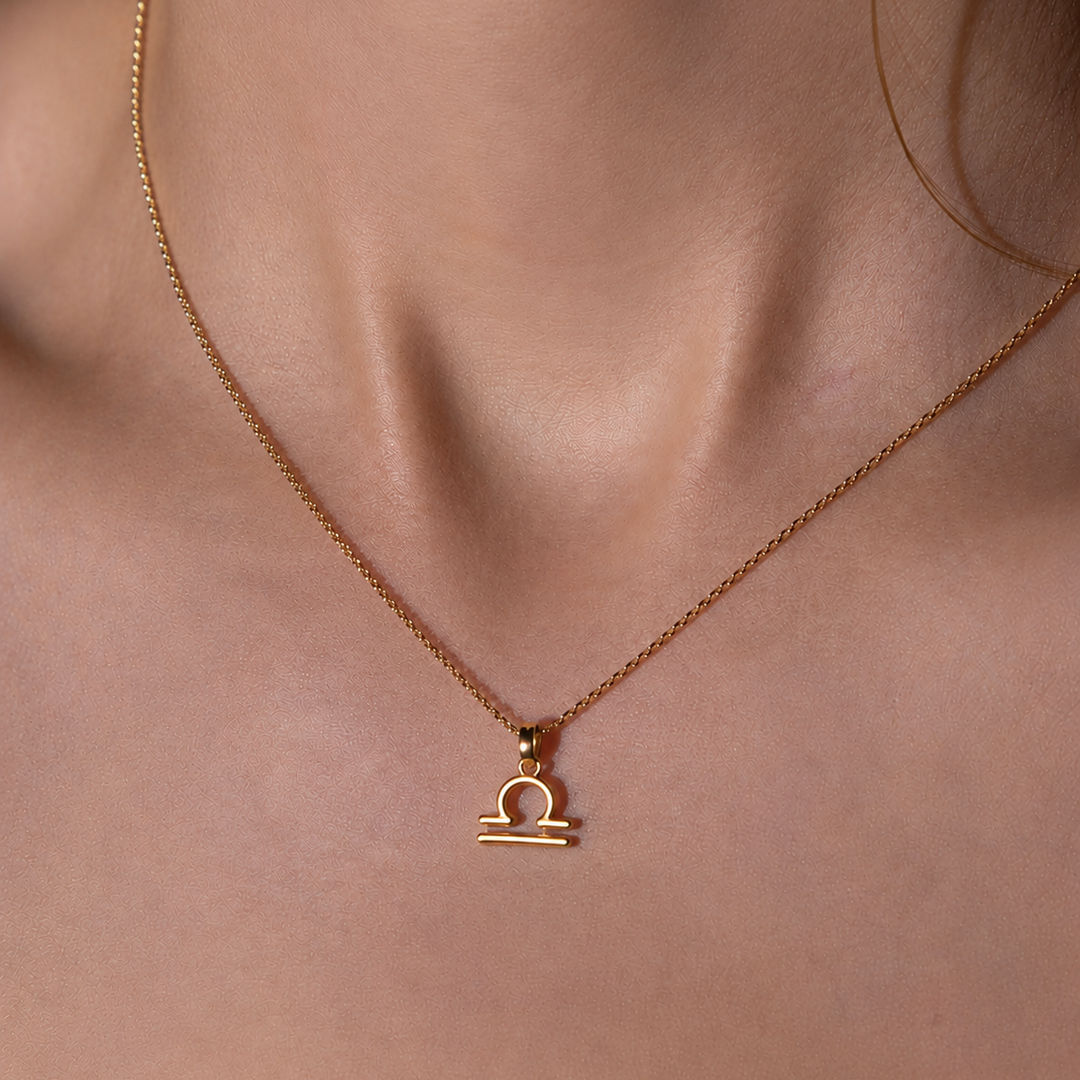 Gold necklace with Libra zodiac pendant on a person's neck