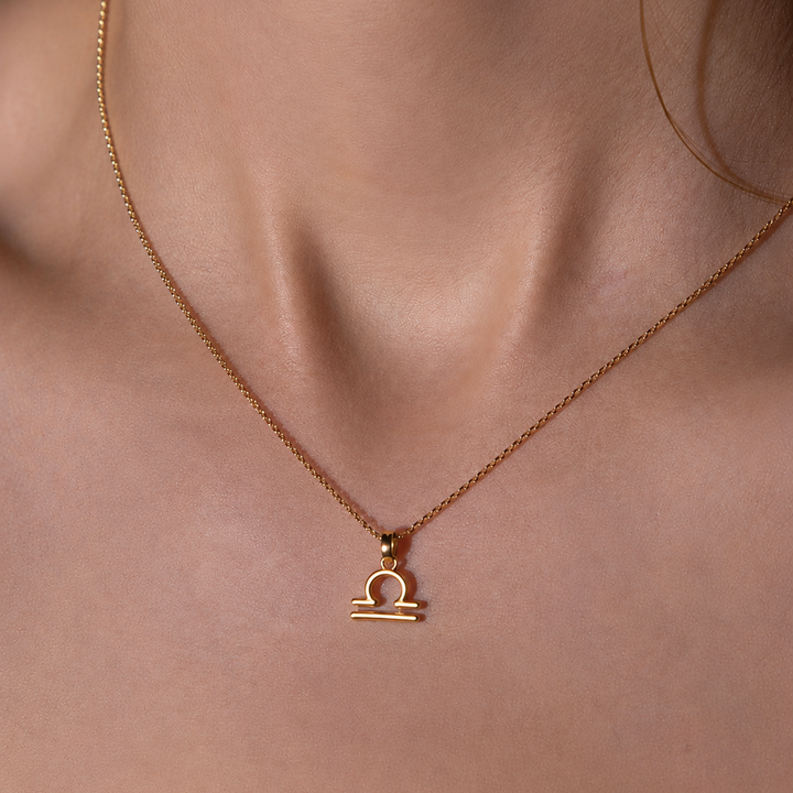 Gold necklace with Libra zodiac pendant on a person's neck