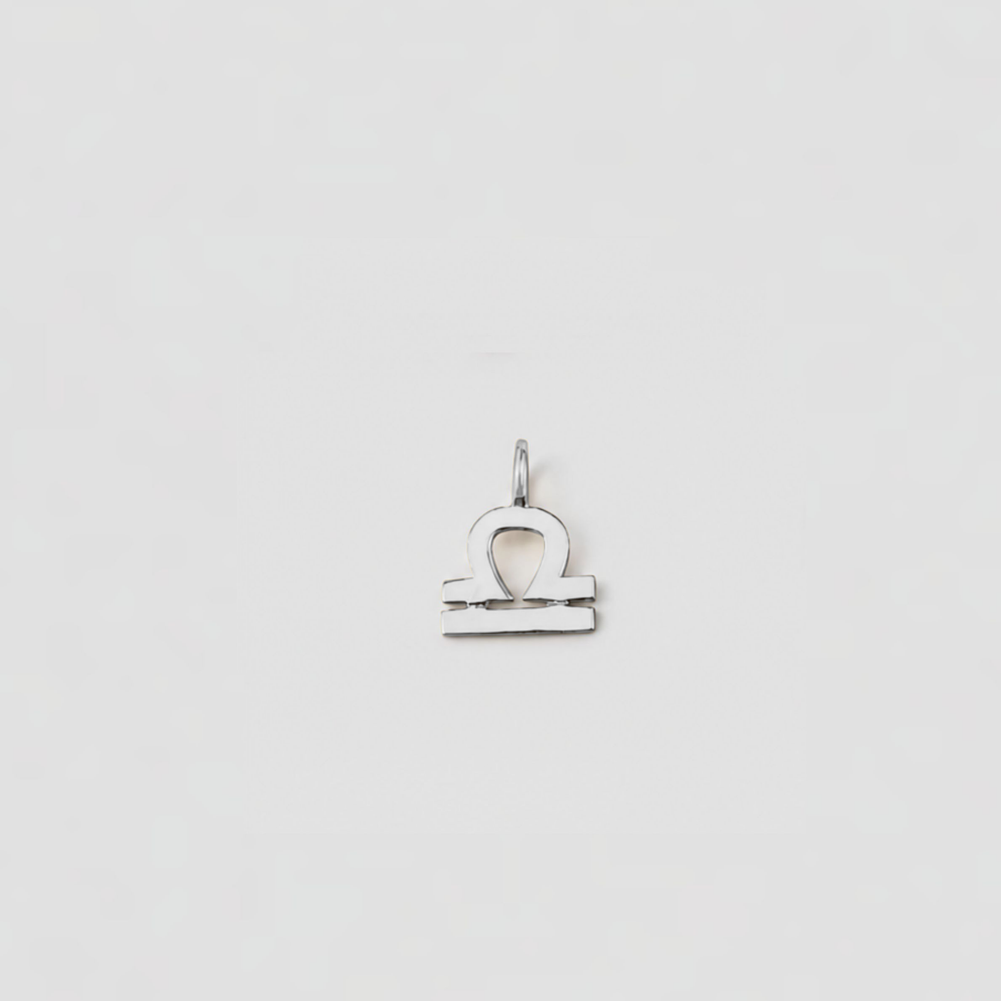 Silver Libra zodiac sign pendant on a light gray background