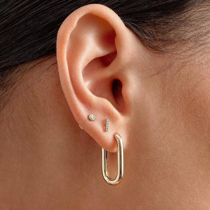 Close-up of an ear wearing a gold hoop earring with a small diamond.