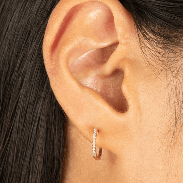 Close-up of an ear wearing a diamond hoop earring with dark hair.