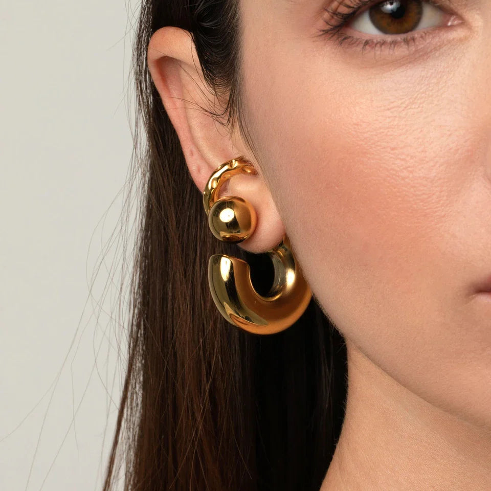 Close-up of a person wearing gold hoop earrings with a neutral background