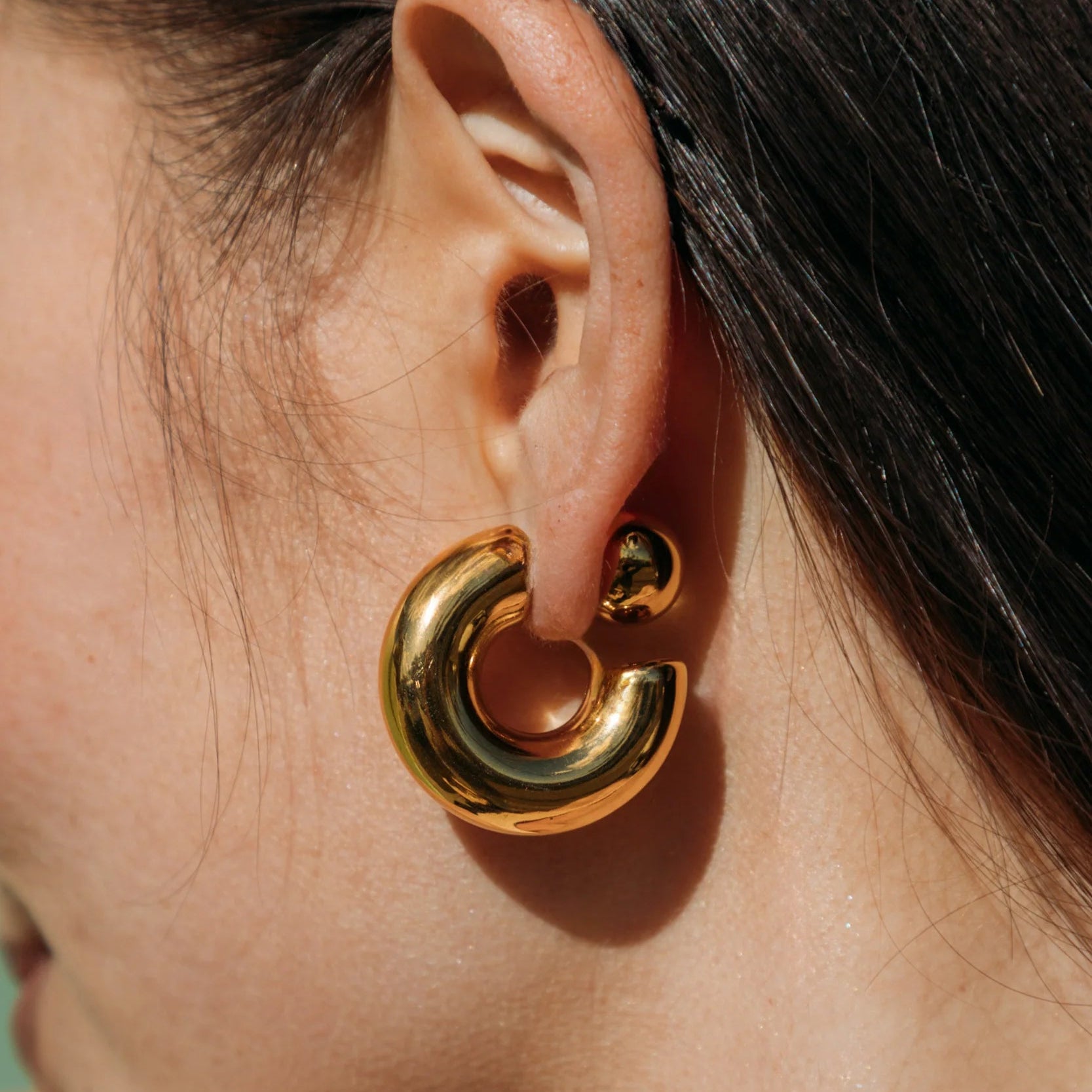 Close-up of a gold hoop earring worn by a person with dark hair.
