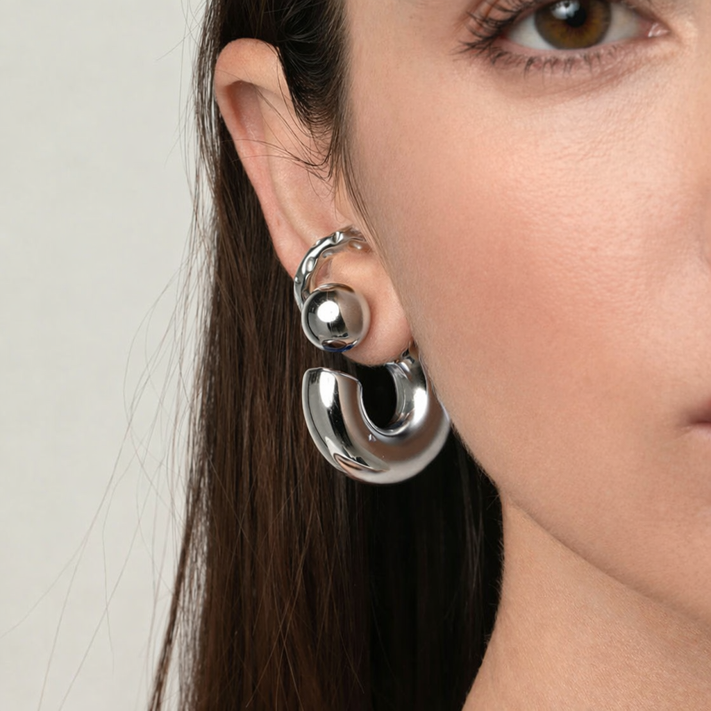 Close-up of a person wearing silver hoop earrings with a neutral background