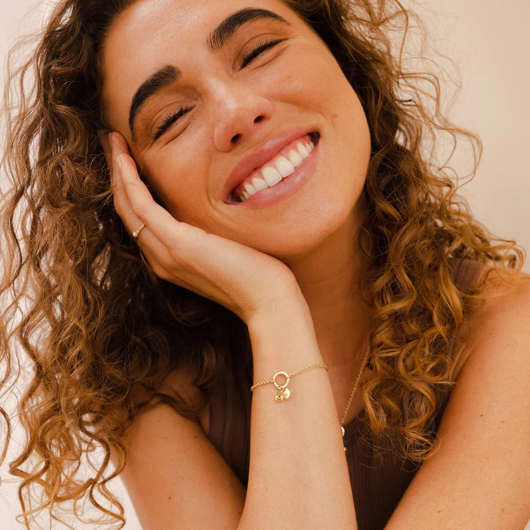 Woman with curly hair smiling and resting her head on her hand against a beige background