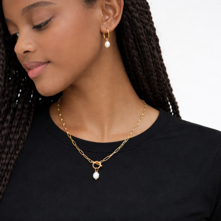 Woman wearing a gold chain necklace with pearl pendants on a plain background