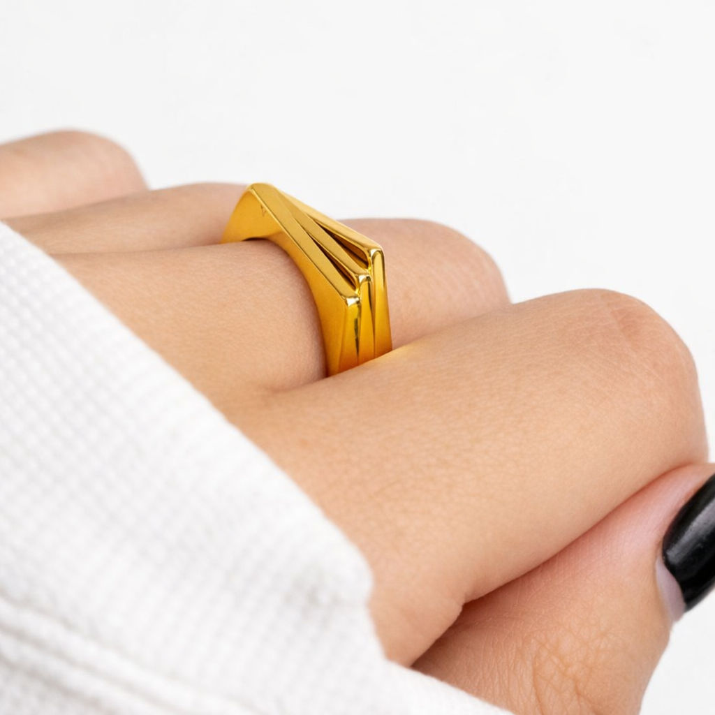 Gold geometric ring on a person's finger with a white background