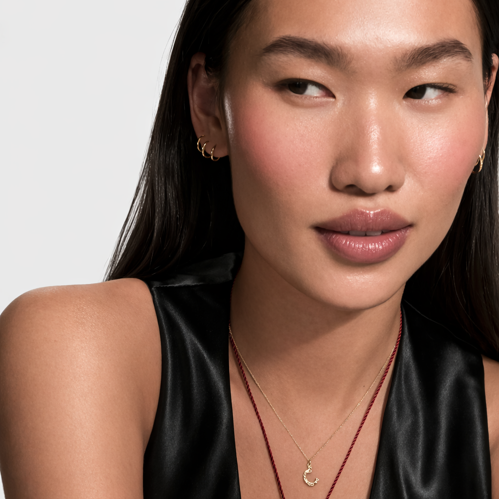 Woman wearing a black sleeveless top with layered necklaces against a white background
