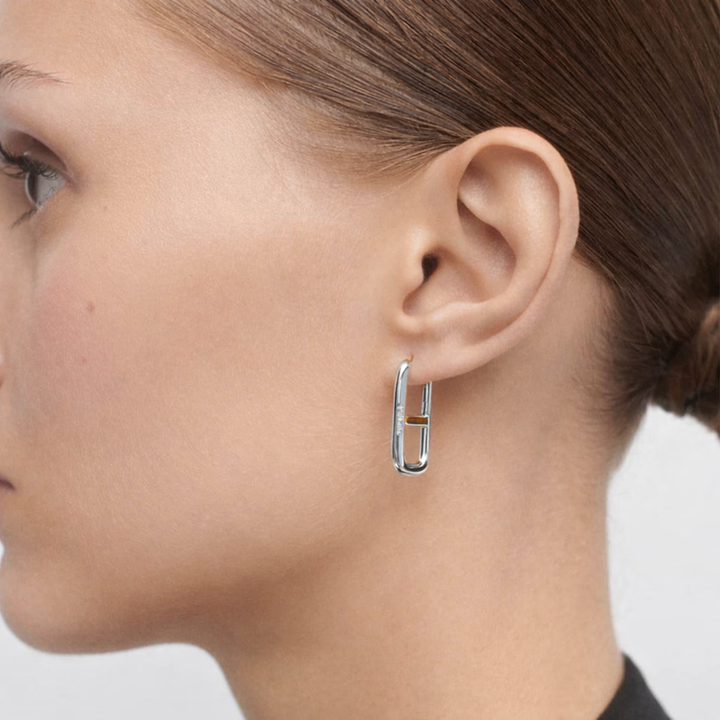 Close-up of a woman's ear wearing a silver hoop earring with a neutral background