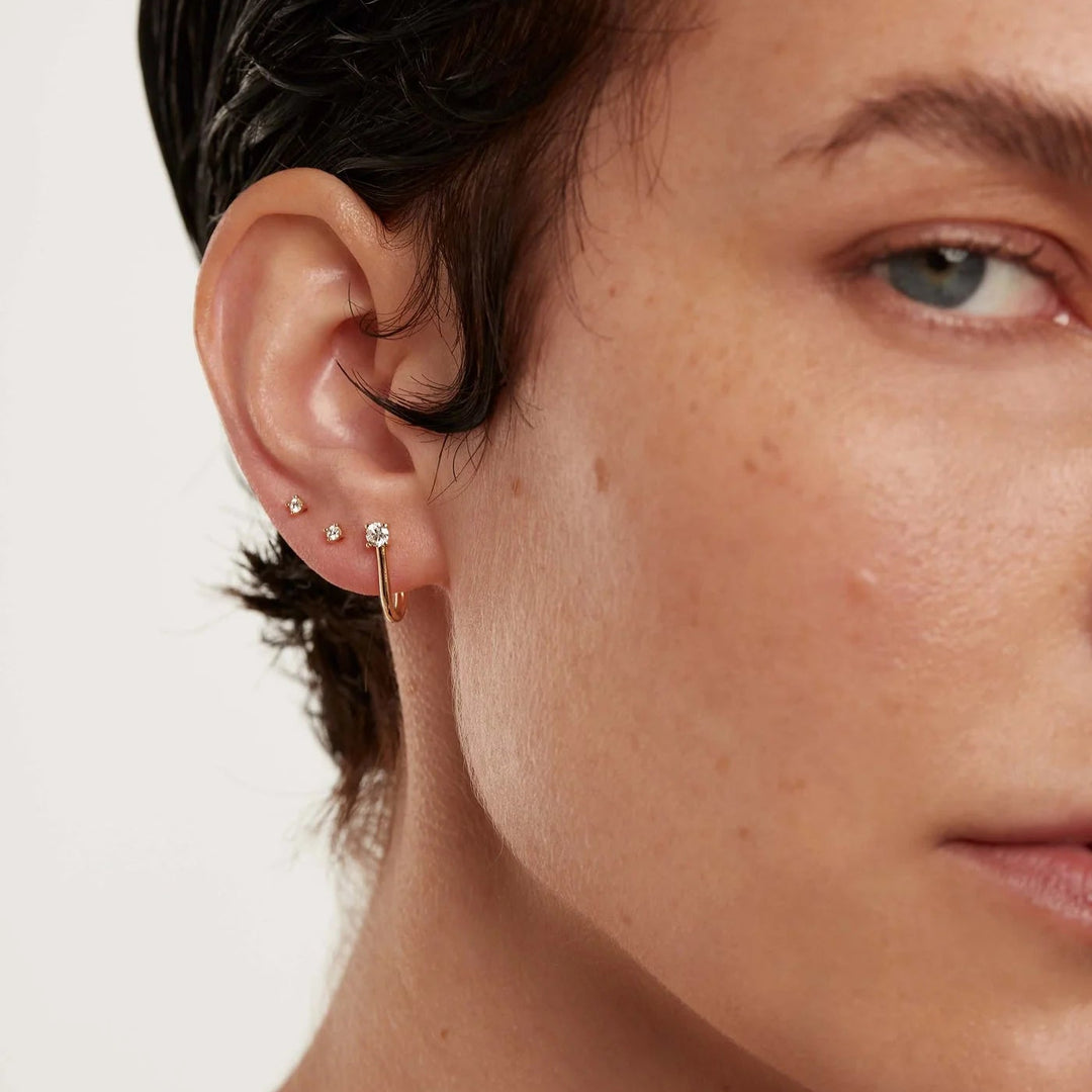 Close-up of a person wearing a gold earring with a small round stone.
