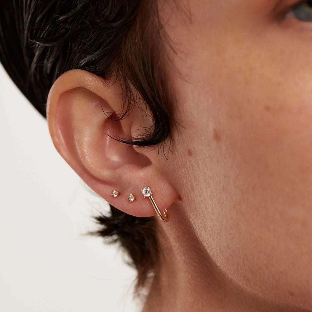 Close-up of an ear with gold earrings on a neutral background