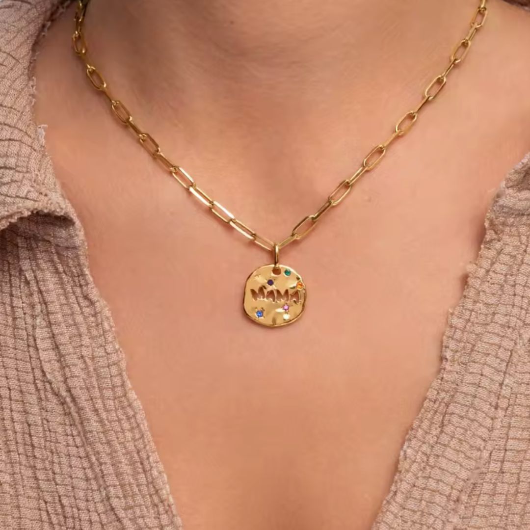 Gold necklace with a 'MAMA' pendant on a person wearing a textured beige top.